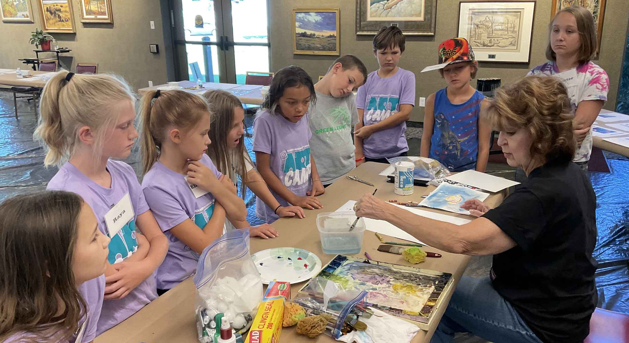 Younger campers watch the instructor demonstrate watercolor techniques.